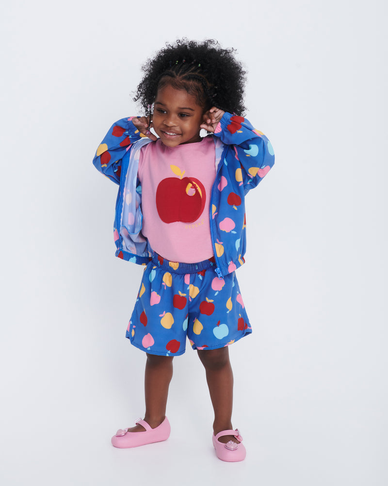 Child model in blue shorts and pink shirt wearing a pair of pink Soft Ballerina Princess baby flats with a pink heart on top