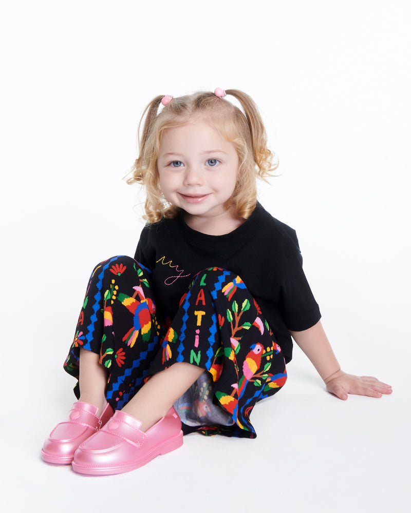 Child model in a black patterned pant set wearing a pair of metallic pink Royal Love baby loafers