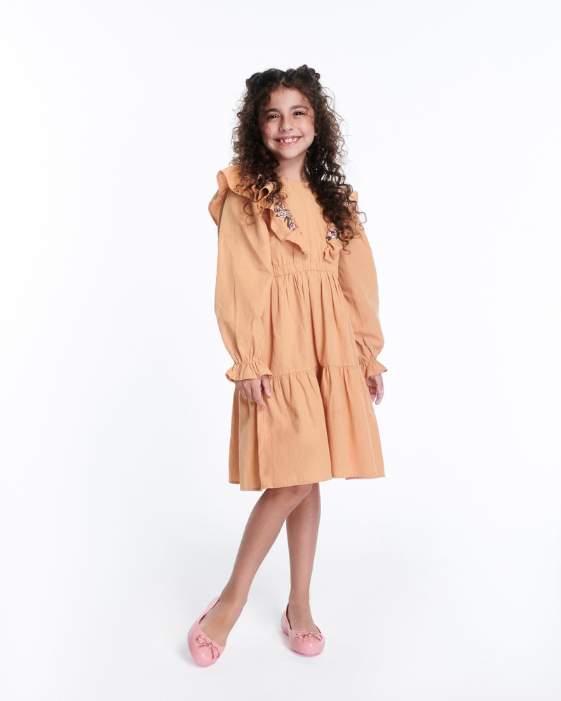 Child model in a peach dress wearing a pair of pink Sweet Love Chrome kids flats with metallic pink bow