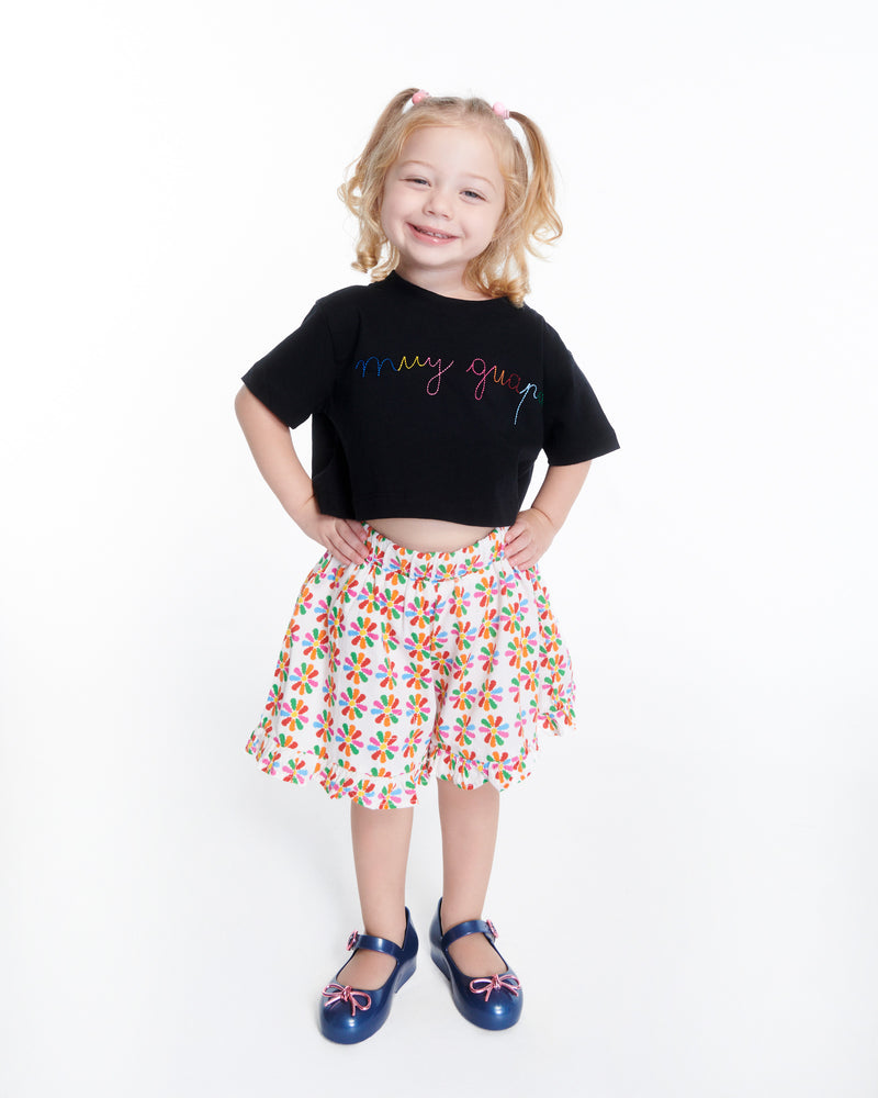 Child model in a skirt and black shirt wearing a pair of blue Sweet Love Chrome baby flats with metallic pink bow and buckle