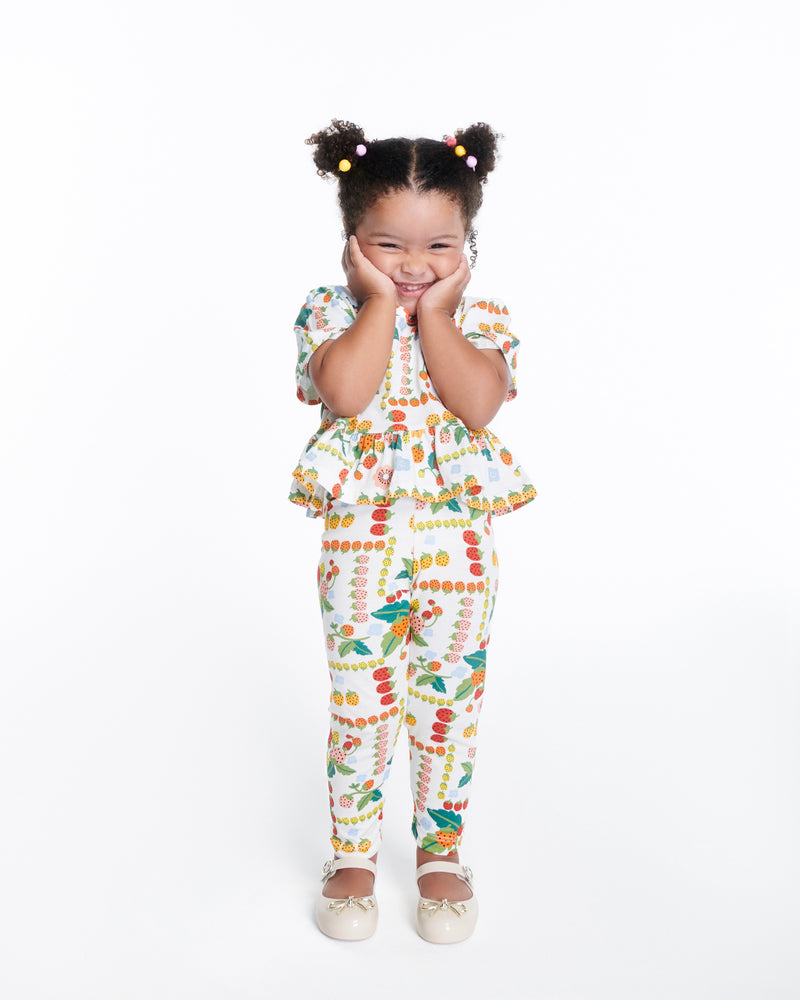 Child model in a pant set wearing a pair of beige Sweet Love Chrome baby flats with metallic gold bow and buckle