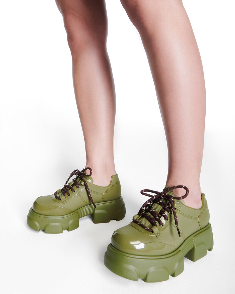 Model's legs wearing a pair of army green Camp platform Sneakers with brown laces