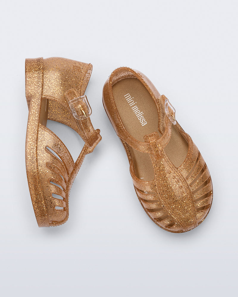 Side and top view of a pair of glitter gold Aranha 79 baby flats with buckle