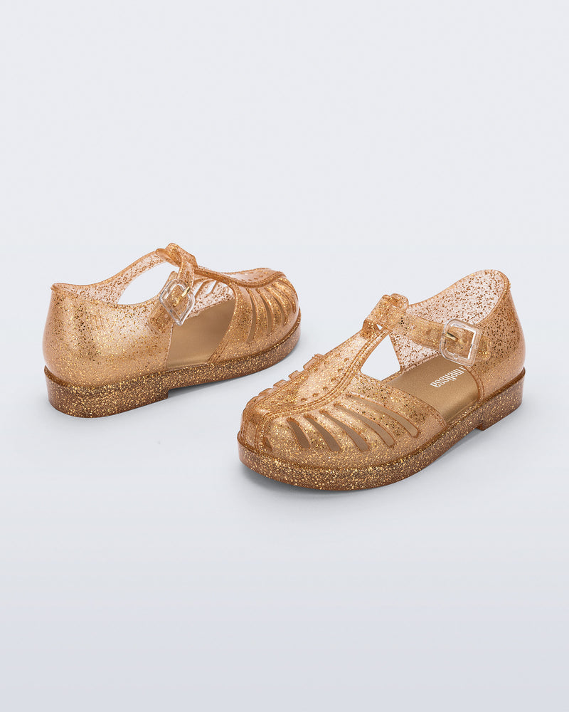 Side and angled view of a pair of glitter gold Aranha 79 baby flats with buckle