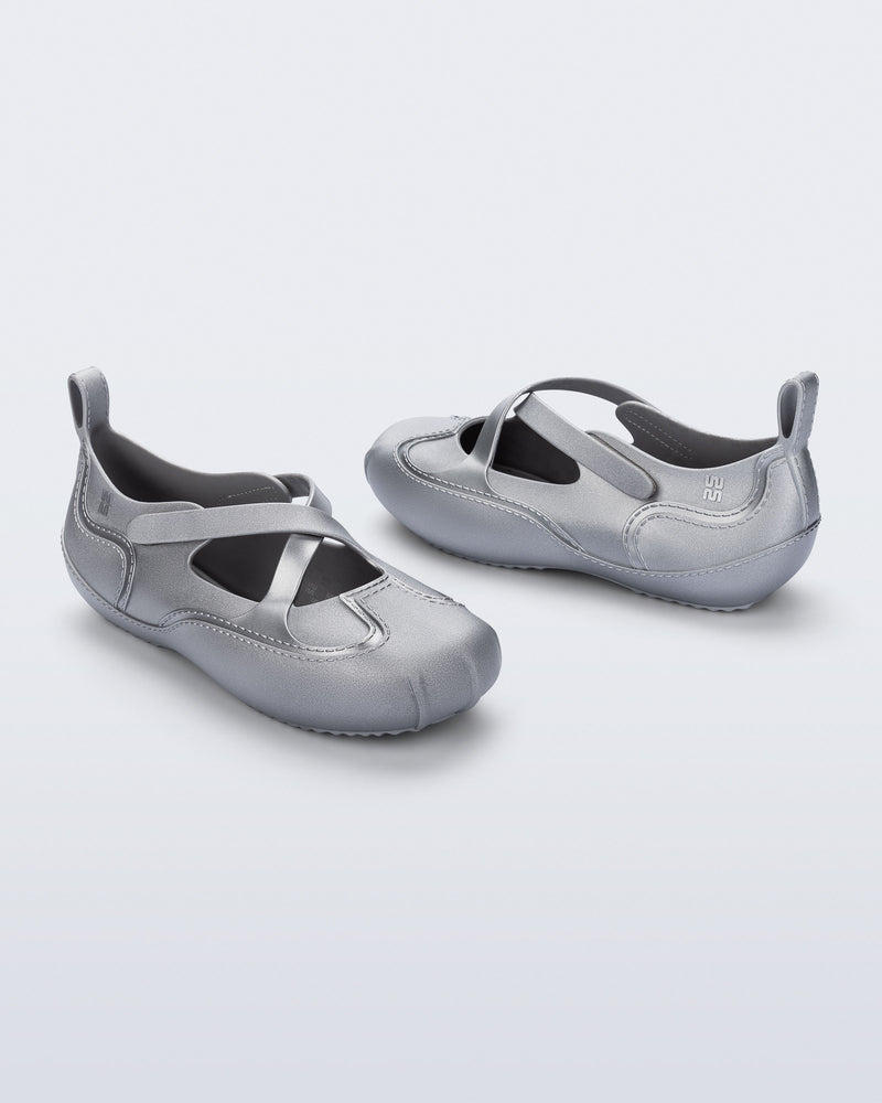 Back and angled view of a pair of silver Aira flats with top straps