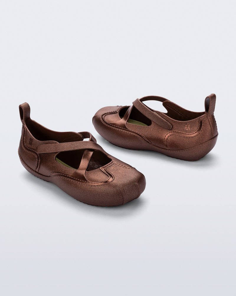 Back and angled view of a pair of bronze Aira flats with top straps