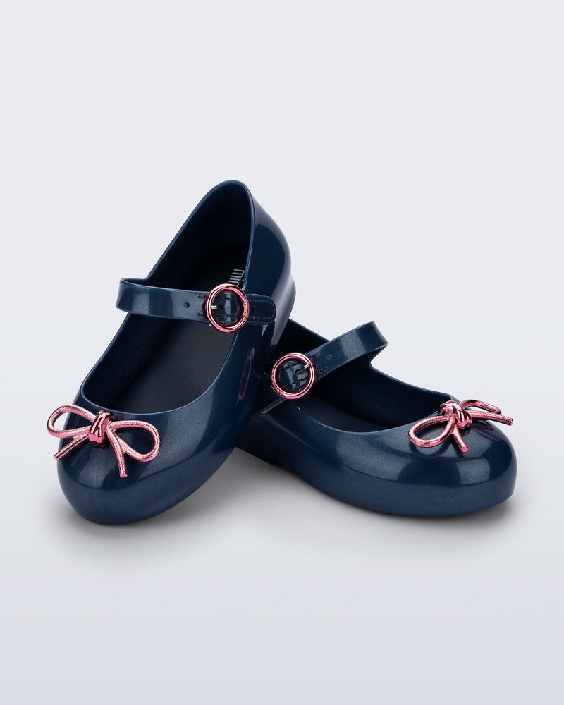 Angled view of a pair of blue Sweet Love Chrome baby flats with metallic pink bow and buckle