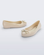 Side and angled view of a pair of beige Sweet Love Chrome kids flats with metallic gold bow