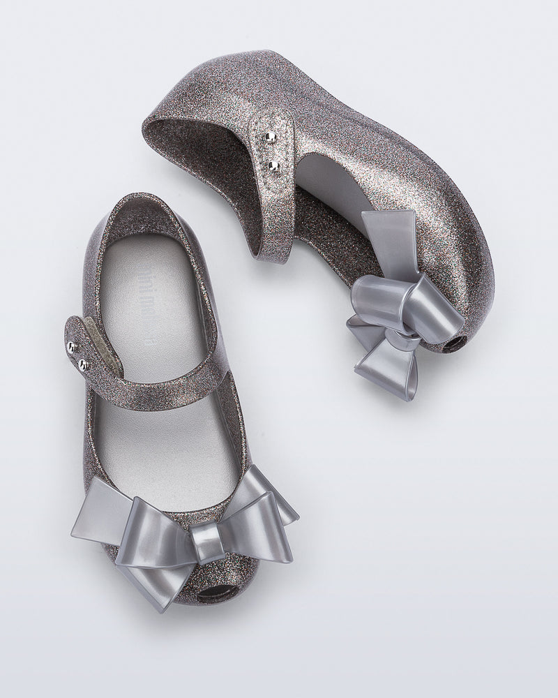 Top and side view of a pair of silver glitter Ultragirl Classy baby flats with silver bow