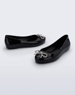 Side and angled view of a pair of black Sweet Love Chrome kids flats with metallic silver bow
