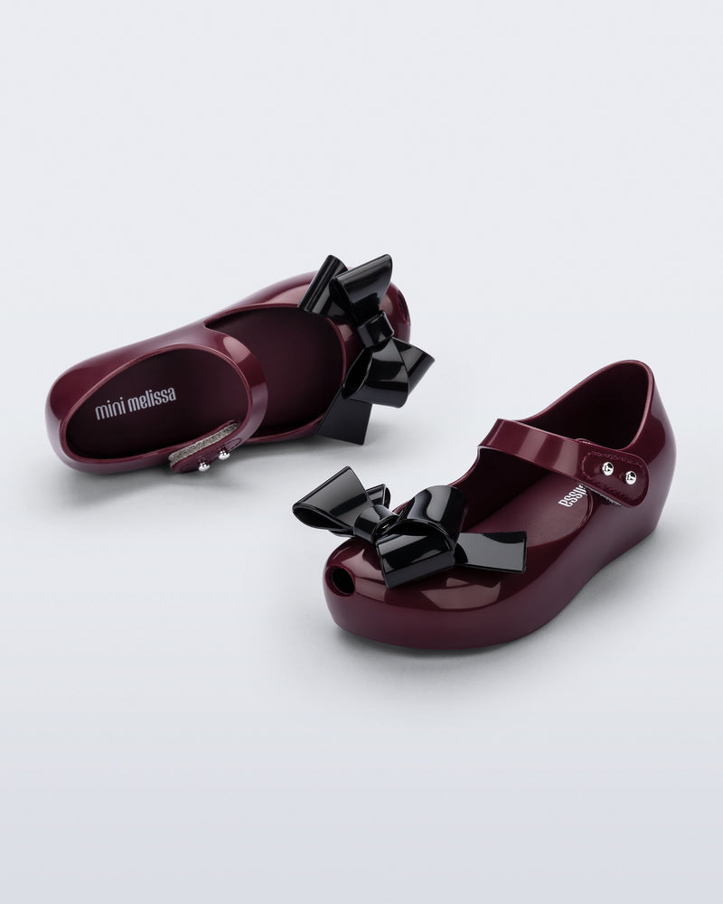 Top and angled view of a pair of burgundy Ultragirl Classy baby flats with black bow