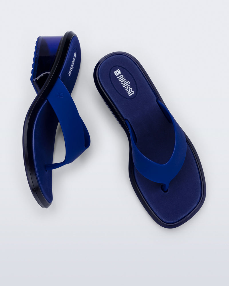 Top and side view of a pair of blue Margot flip flops with clear blue low heel