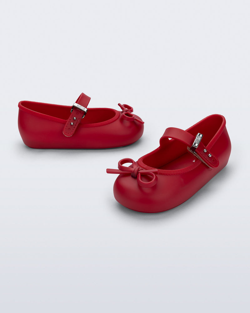 Side and angled view of a pair of red Soft Ballerina Delicate Bow baby flats with top strap and bow
