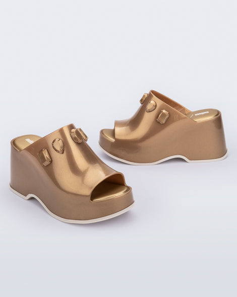 Angled and side view of a pair of metallic gold Patty Stones + Undercover platform open toe mules with beige sole and stone embellishments on upper.