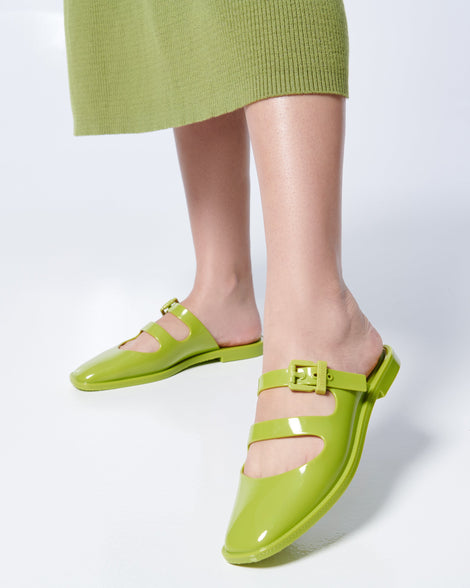 Model's legs in a green skirt wearing a pair of green Anastasia mule slides