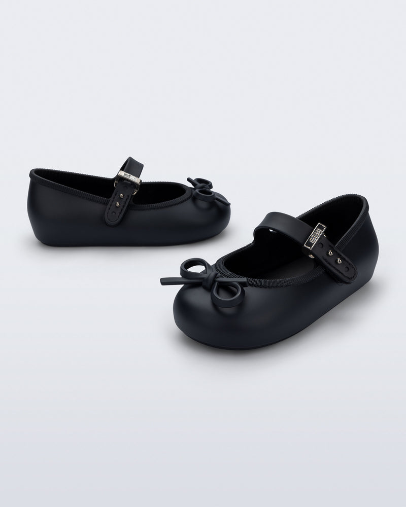 Side and angled view of a pair of black Soft Ballerina Delicate Bow baby flats with top strap and bow