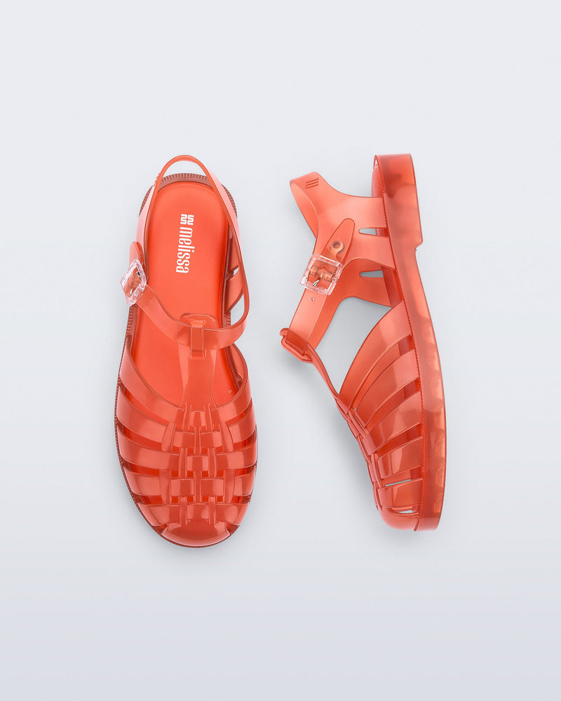Top and side view of a pair of transparent orange Possession fisherman sandals