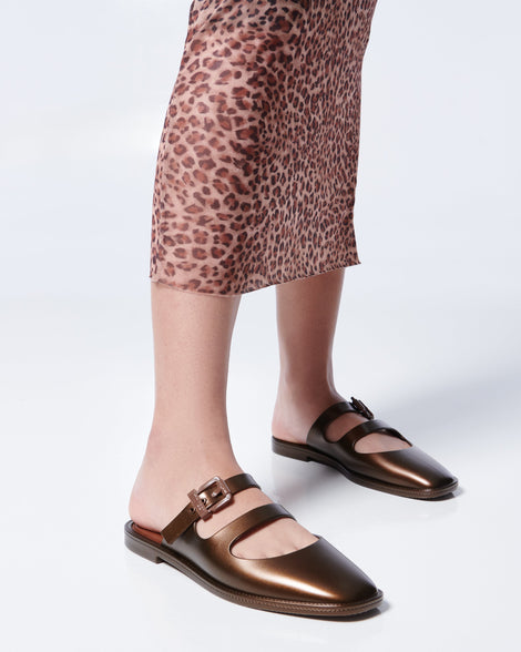 Model's legs in a leopard print skirt wearing a pair of bronze Anastasia mule slides