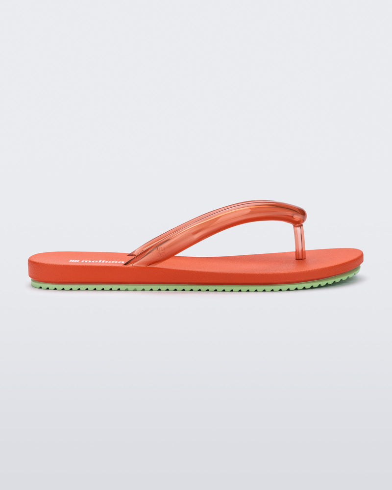 Side view of a orange Flip Flop Airflow sandal with a clear orange strap and green bottom