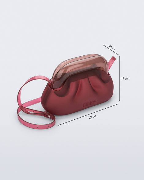 Angled view of a small red bag with clear brown clutch and long strap with measurements 27 cm x14 cm x 17 cm
