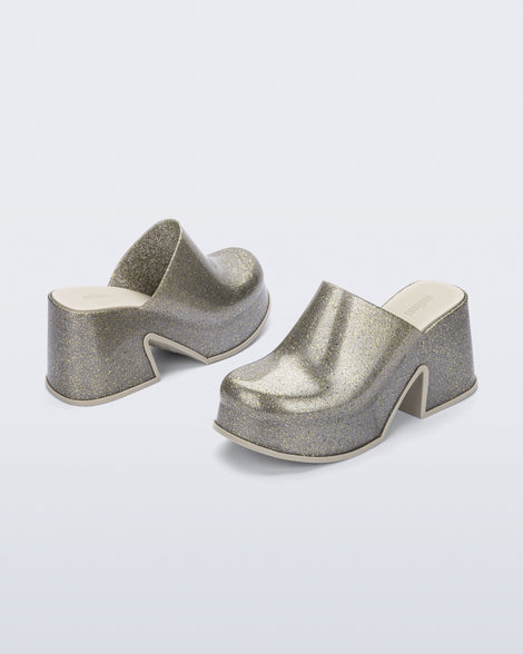 Side and back angled view of a pair of golden glitter silver Mia mules with white sole