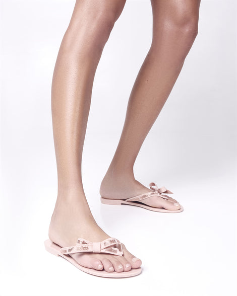 Model's legs wearing a pair of light pink Harmonic M Lover adult flip flop with Melissa logo on strap