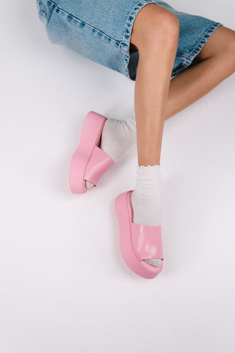A model in jean shorts and pink socks wearing a pair of pink Melissa Becky platform slides.
