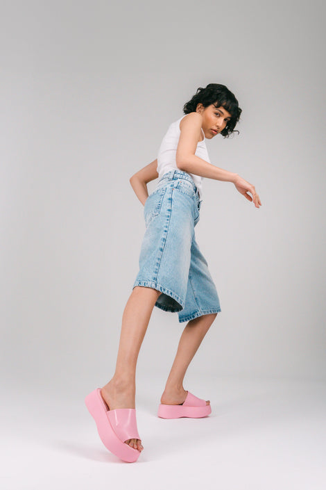 A model in jean shorts and pink socks with white tank top wearing a pair of pink Melissa Becky platform slides.