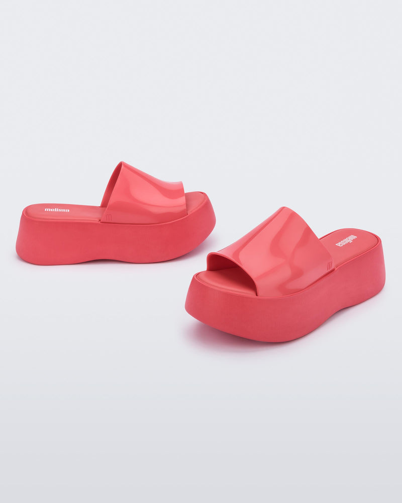 Angled view of a pair of Melissa Becky platform slides in bright pink colorway. Single thick slide strap with open toe.