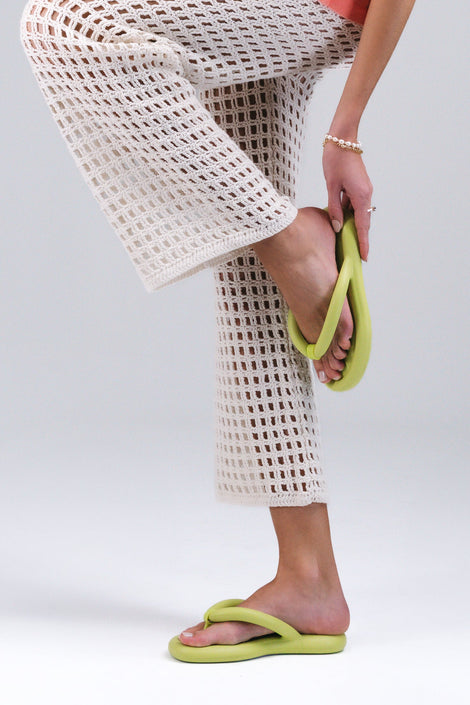 A model's legs in white pants wearing a pair of lime green Melissa Free Flip Flops with puffer-like straps.