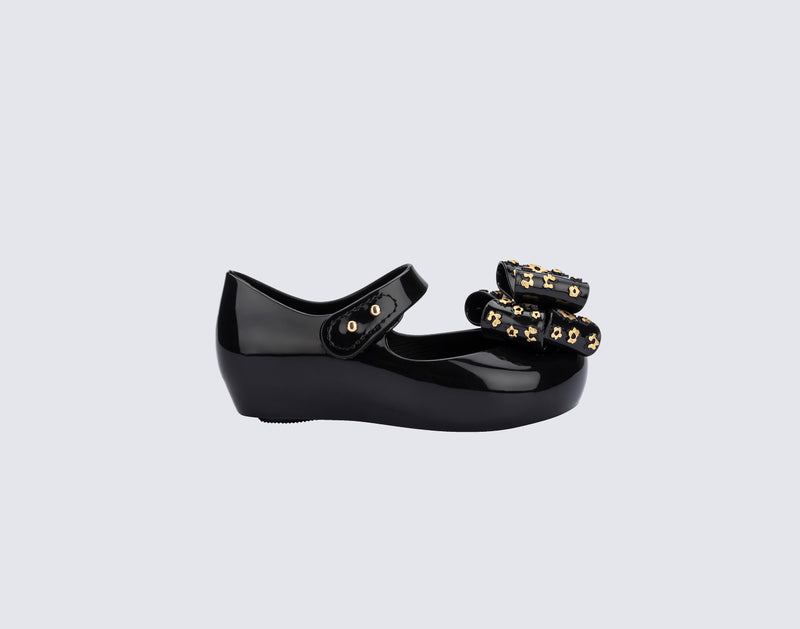 Top and angled view of a pair of black Ultragirl Sweet X baby flats with a bow that has chrome flowers on it