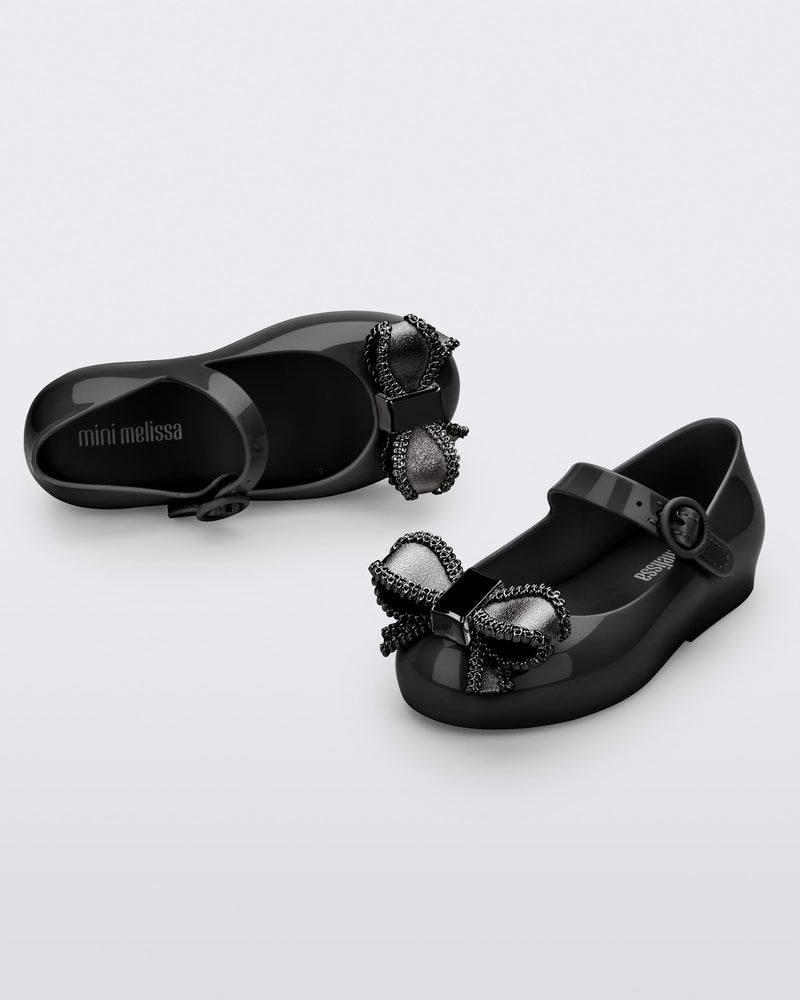 Top and angled view of a pair of black Mini Melissa Sweet Love baby mary jane flats with a metallic gray bow.