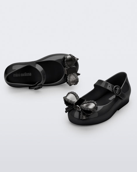 Top and angled view of a pair of black Mini Melissa Sweet Love baby mary jane flats with a metallic gray bow.