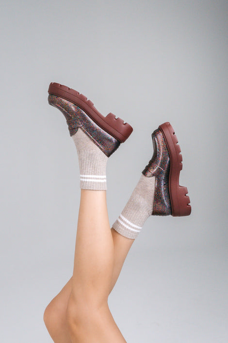Model's legs in beige socks wearing a pair of Melissa Royal loafers in glitter multicolor with a brown platform sole.