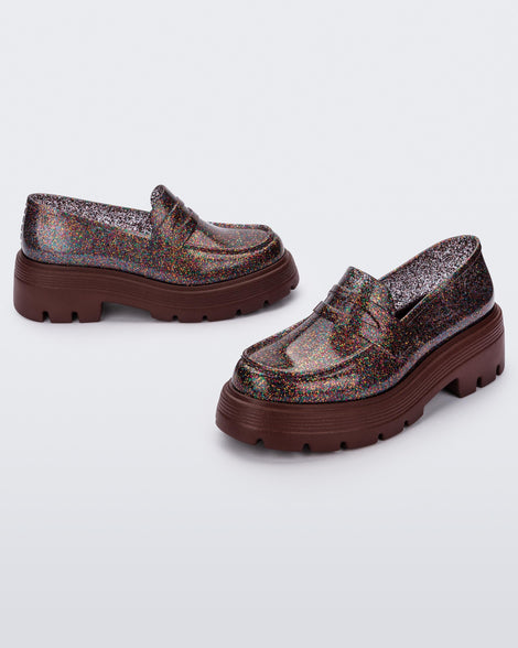 Angled view of a pair of Melissa Royal loafers in glitter multicolor with a brown platform sole.