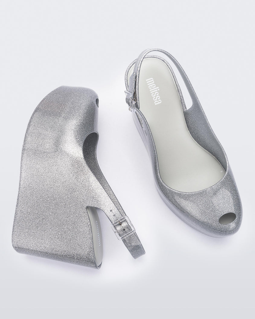 Side and top view of a pair of clear glitter Melissa Groovy wedge platform slingback heels with peep toe.