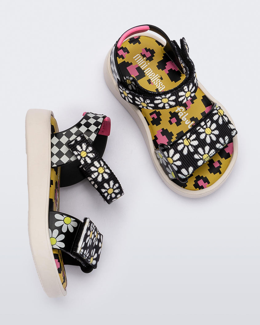 Top and side view of a pair of white, black and yellow patterned Mini Melissa Pula Pula + Fabula sandals.