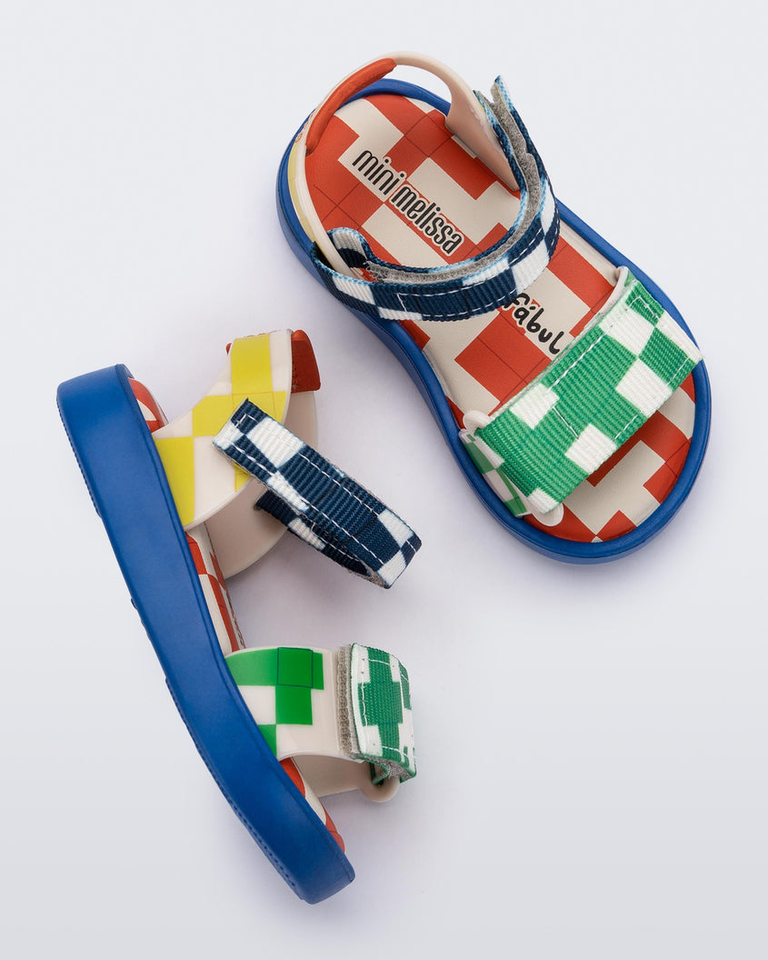 Top and side view of a pair of blue, yellow, green and beige patterned Mini Melissa Pula Pula + Fabula sandals.