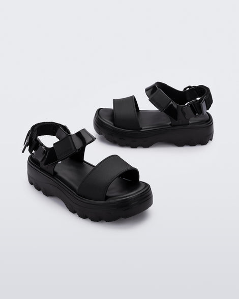 Angled view of a pair of Mini Melissa Kick Off platform sandals in black with adjustable velcro ankle straps