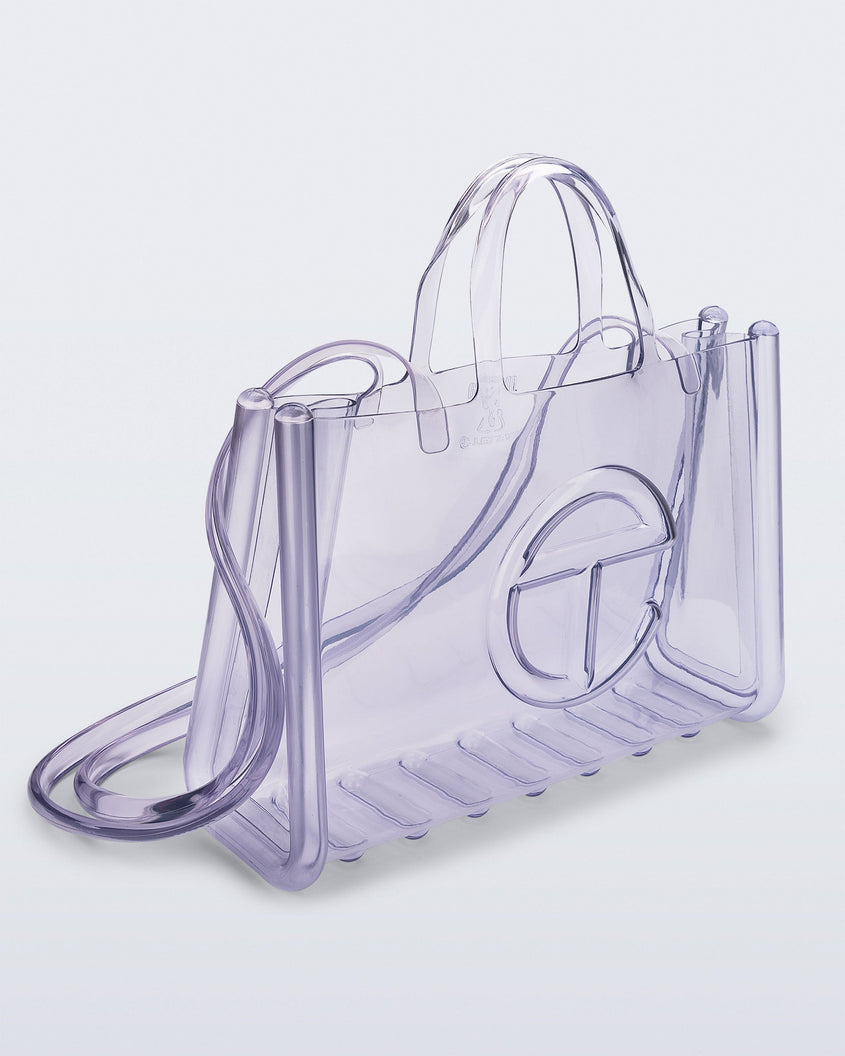 Angled view of a clear Melissa Large Jelly Shopper + Telfar bag with handles and a body strap
