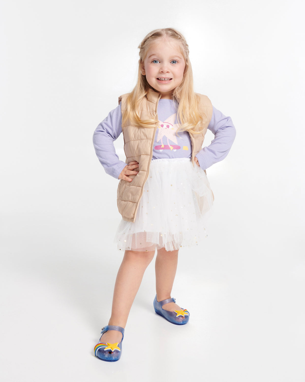 Child model in a purple shirt and white skirt wearing a pair of glitter blue Ultragirl Colors baby flats with yellow star and rainbow on top
