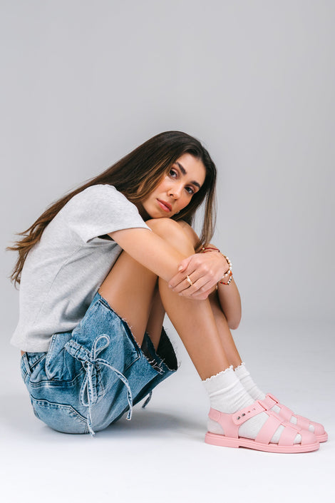 Model in jean shorts and white shirt with white socks wearing a pair of pink Emma women's sandals.