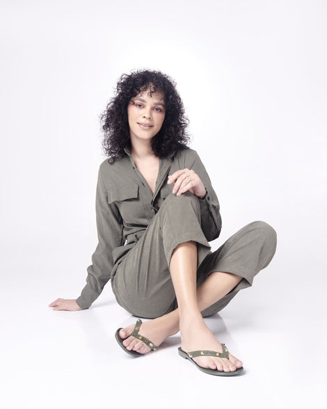 Model in a green outfit wearing a pair of green Melissa Harmonic Studs flip flops with gold studs on the upper.