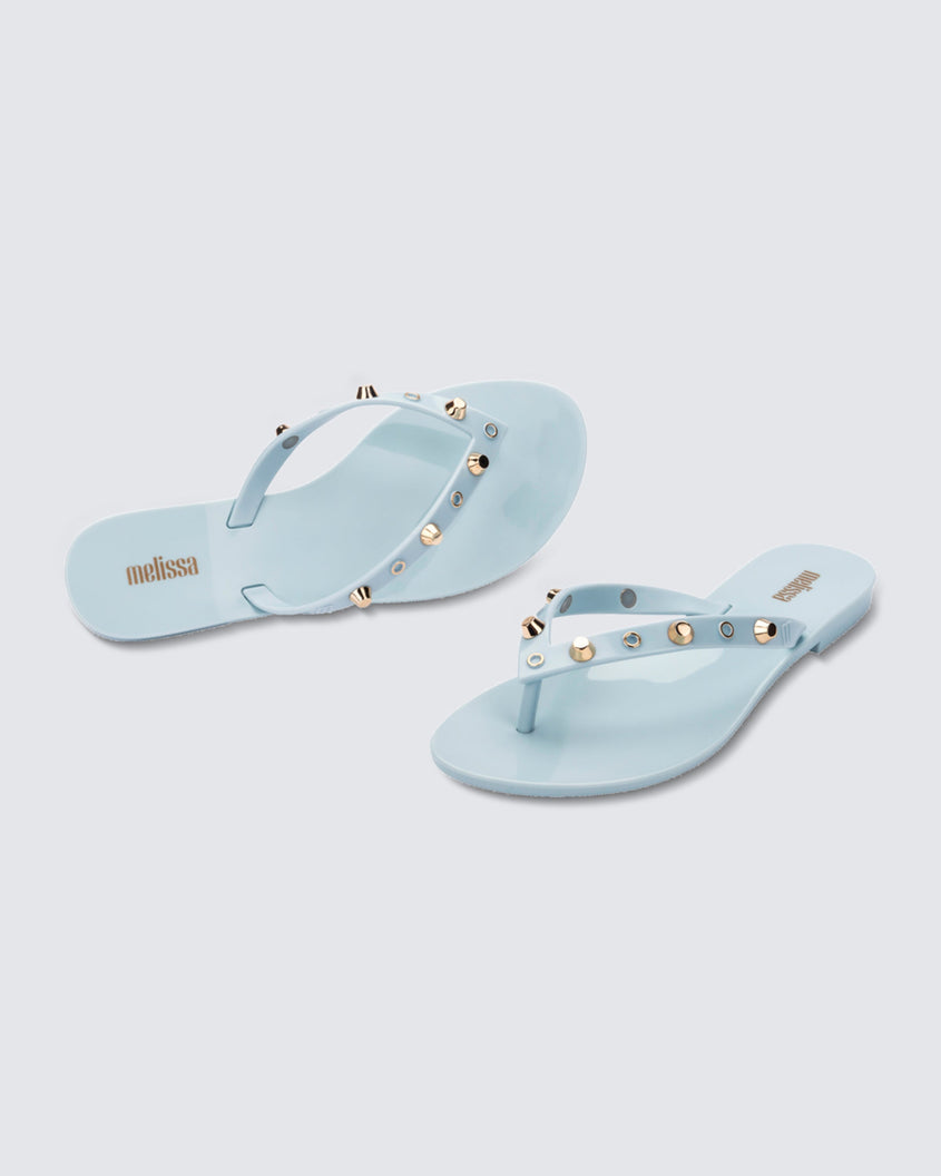 Angled and top view of a pair of blue Melissa Harmonic Studs flip flops with gold studs on the upper.
