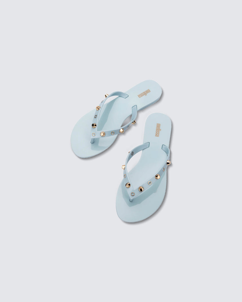 Top view of a pair of blue Melissa Harmonic Studs flip flops with gold studs on the upper.