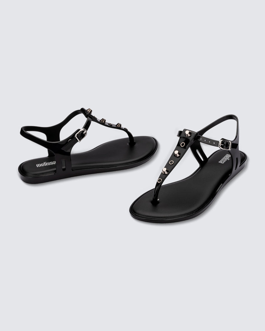 Angled and side view of a pair of black Melissa Solar studs sandals with gold studded t-strap and gold buckle.