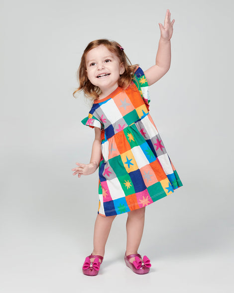 Child model in a multi color dress wearing a pair of glitter pink baby Ultragirl Classic Bow flats