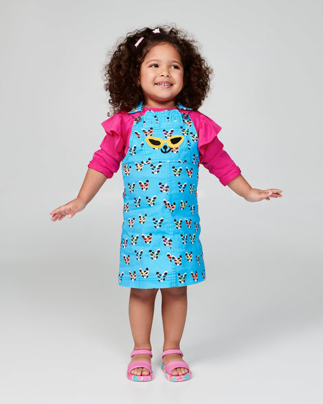 Child model in a blue dress wearing a pair of pink baby Imagine sandals