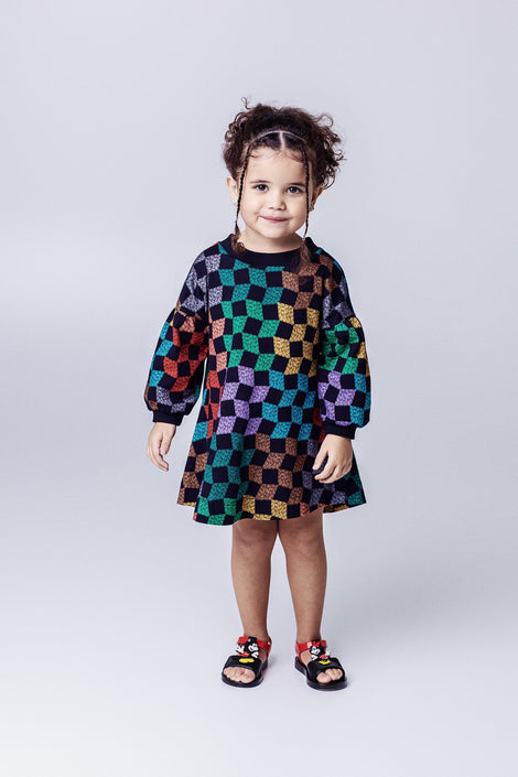 Child model in a black multi-colored dress wearing a pair of black Play Mickey & Minnie sandals with red straps