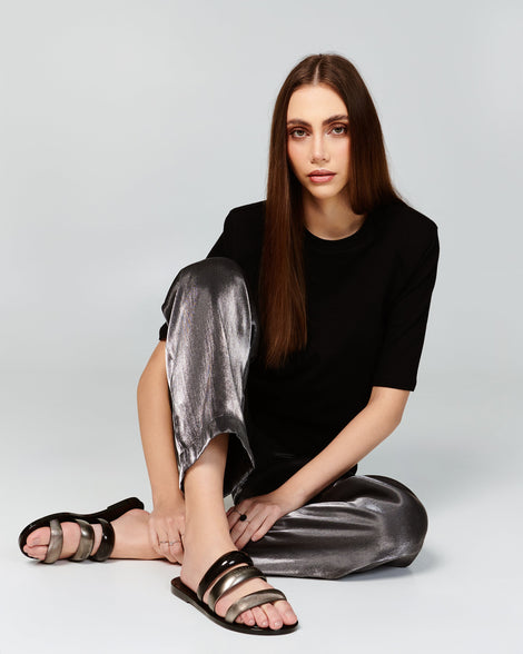 Model in a black shirt and sliver pants wearing a pair of black Eclipse Slides.